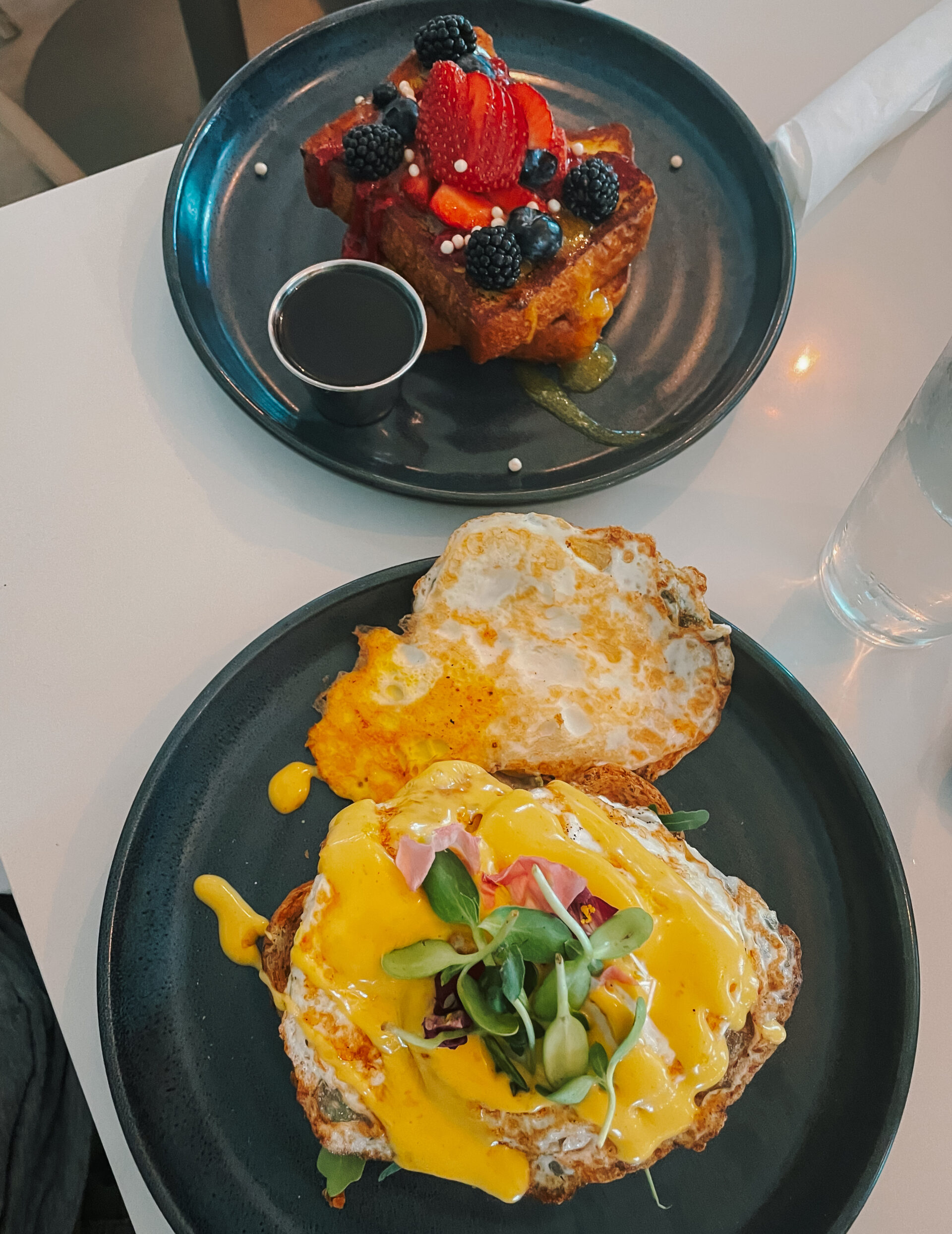 Two plates of food - one with French Toast and fruit and the other with a breakfast egg sandwich