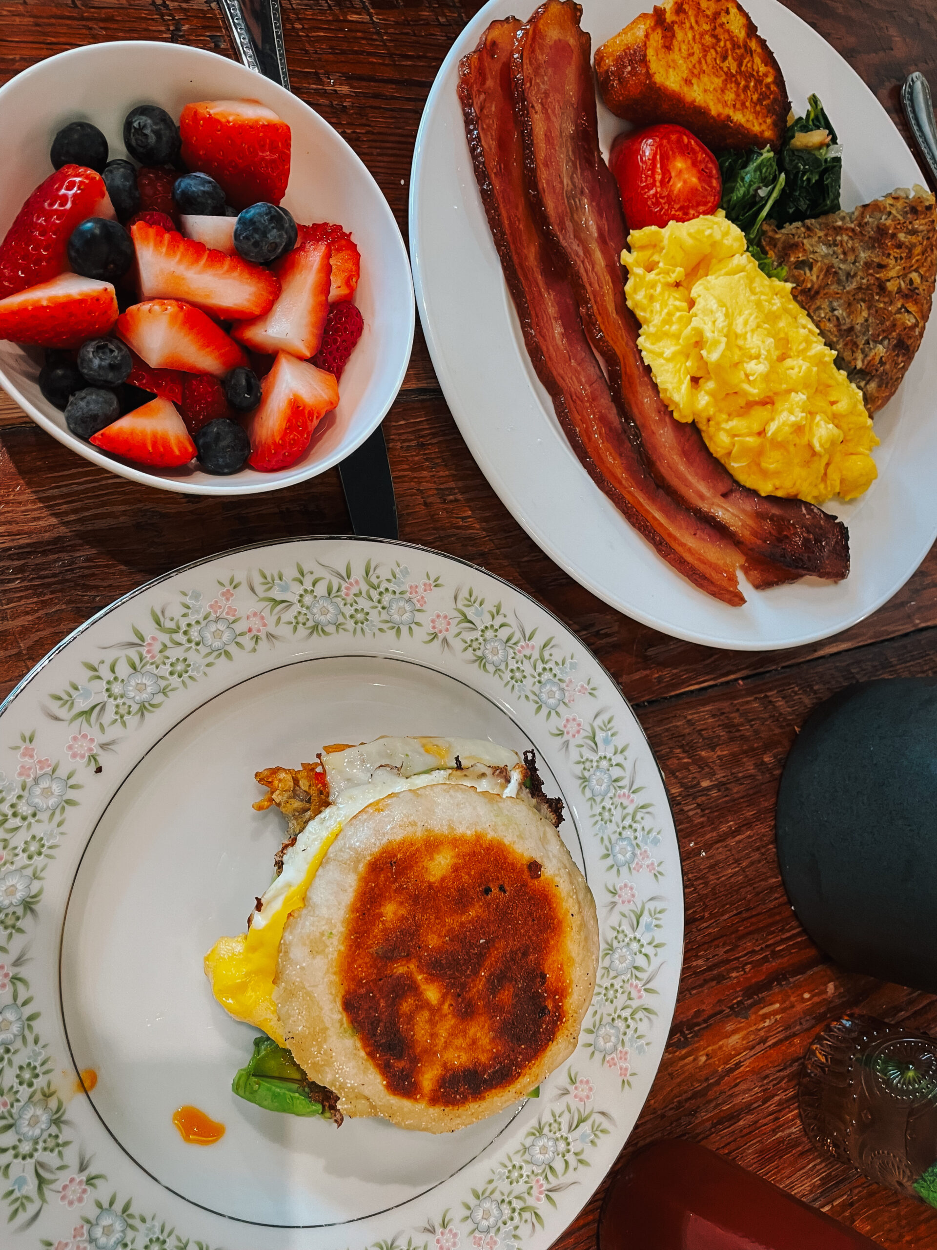 Table with a bowl of fruit and two plates of breakfast foods. 