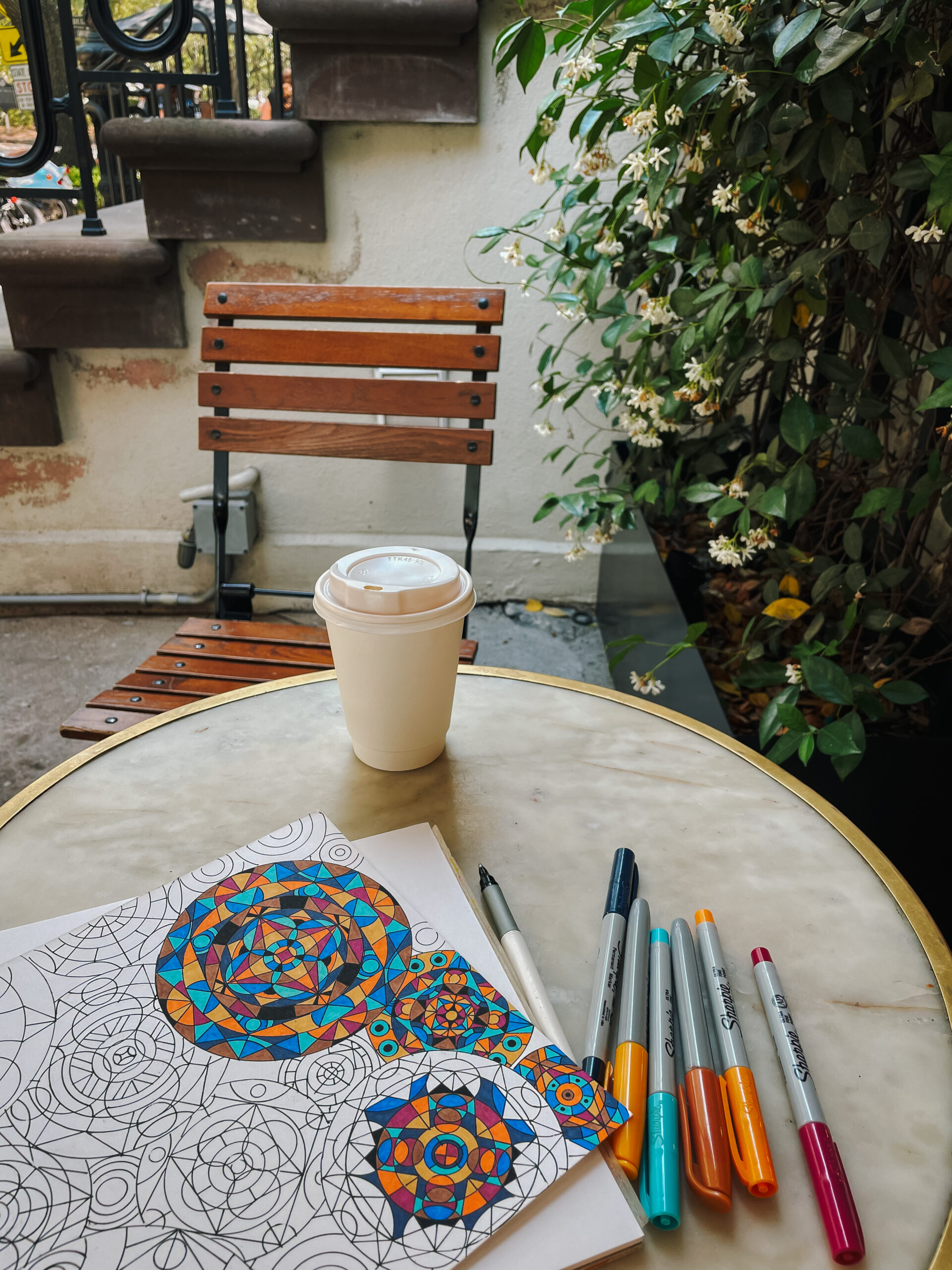 Outdoor table with paper coffee cup and unfinished drawing next to markers