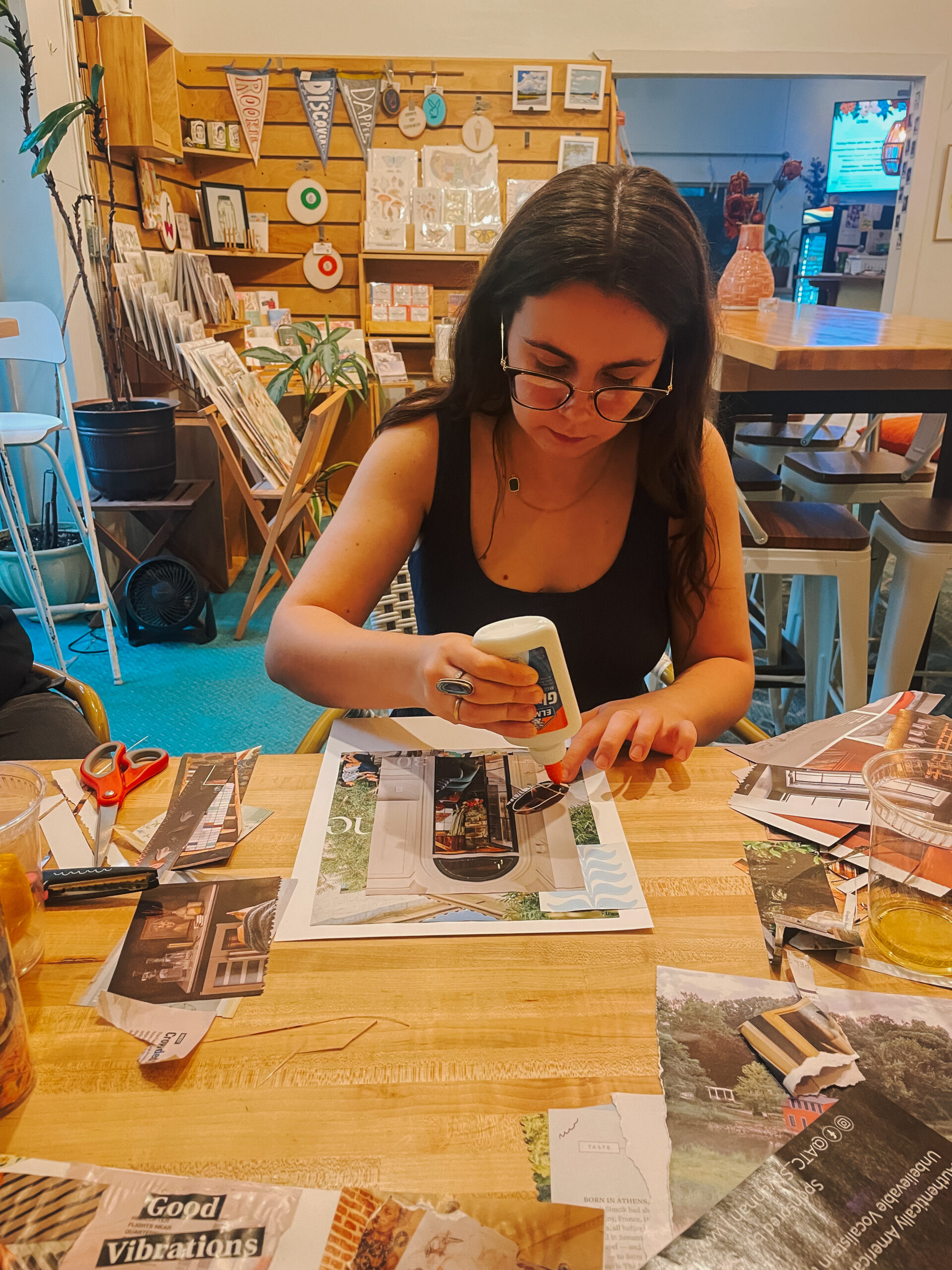 Girl holding bottle of glue while making a collage in cafe